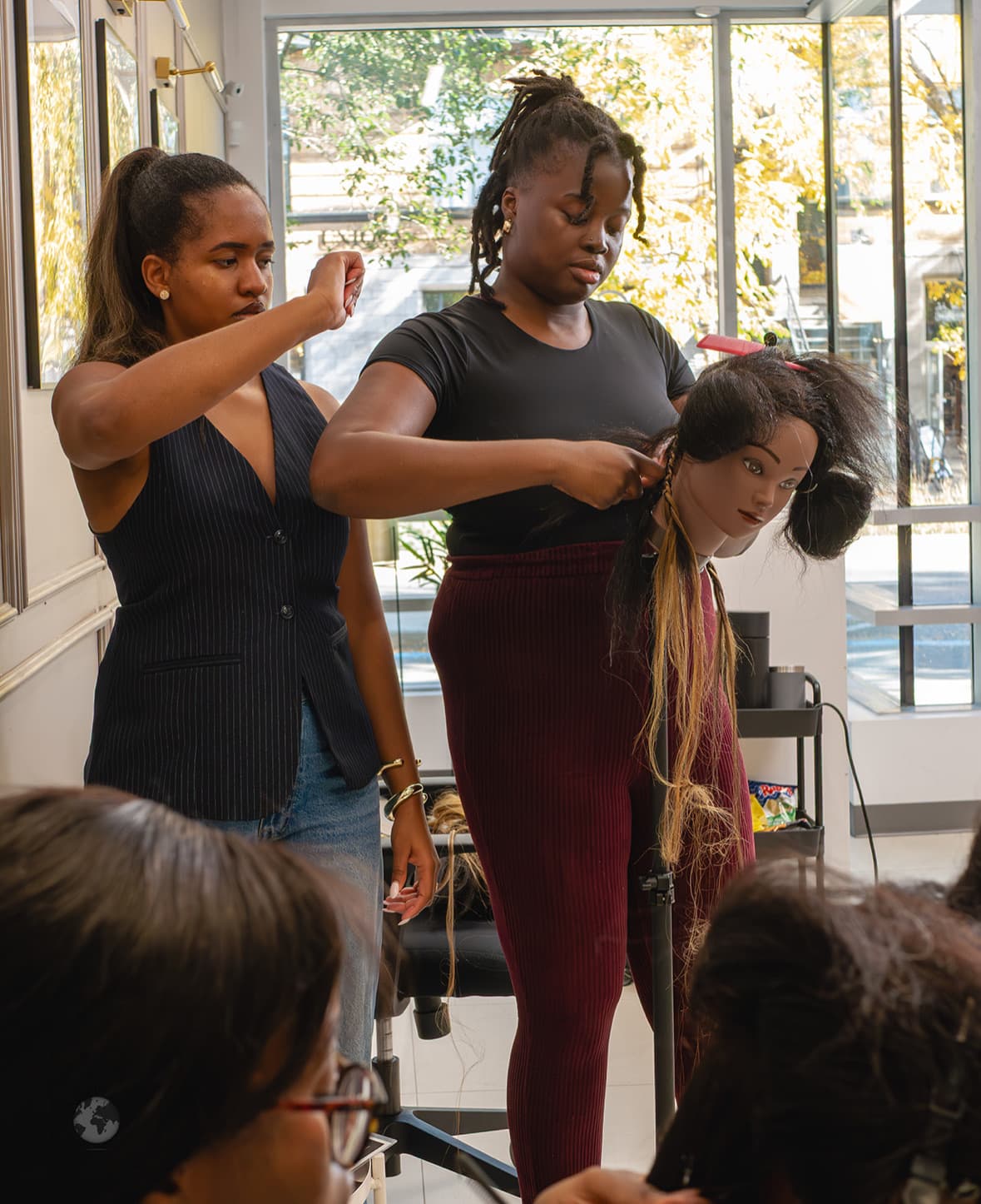 An instructor showing braiding technique on a mannequin head to a student